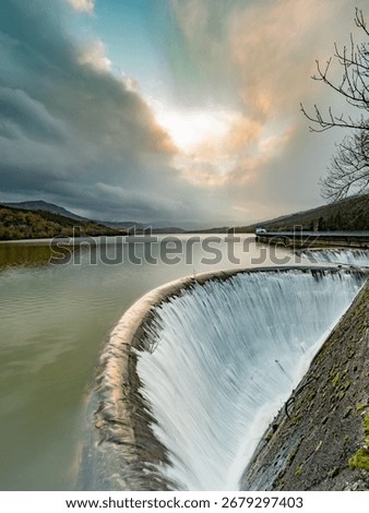 Spillway Waterfall at Sunset with Dramatic Sky - A wide-angle shot of a dam spillway with water cascading into a waterfall under a magnificent, cloudy sky at sunset.