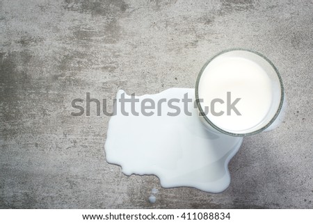 Spilt milk and a glass of milk on a gray concrete table