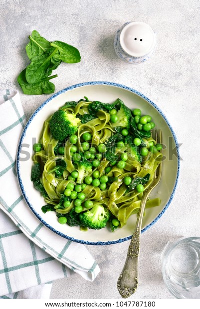 Spinach pasta primavera with green\
vegetables (broccoli, sweet pea and spinach) in a white bowl over\
light slate, stone or concrete background.Top\
view.