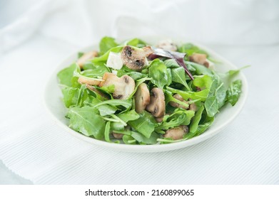 Spinach Salad With Mushrooms And Feta Cheese On A White Plate