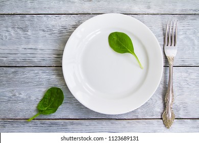 spinach sheet on empty plate on wooden background and fork for simple diet