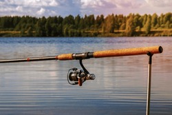 Spinning Fishing Rod Mounted Horizontally On A Prop, Cork Handle And Reel Against River And Forest. Sport Fishing, Hobby, Leisure Time On Vacation Or Weekend