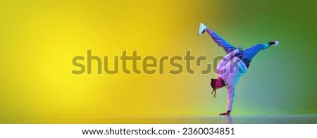 Spinning on one hand. Young man with dreads in casual clothes dancing breakdance against gradient yellow green background in neon. Concept of street style dance, fashion, youth, hobby. Banner. Ad