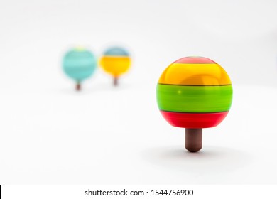 A Spinning Top In Coloured Wood Spins In Balance. Some Colourful Spinning Tops On A White Background Isolated. Copy Space.