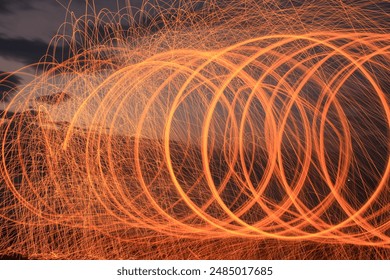 A spiral image created using light trails from sparks, with a twilight sky as a background