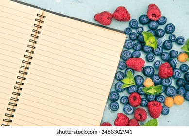 Spiral notebook with blueberries and raspberries. Flat lay from above. Template for writing or presentation mockup. Top view with copy space for text. Summer holiday mood