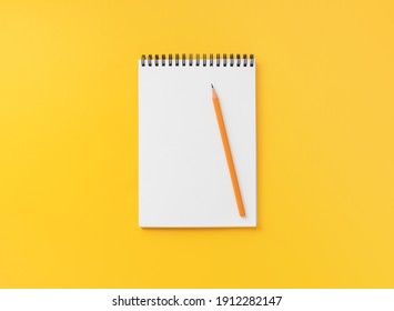 Spiral notebook with pencil on yellow table, top view, flat lay  