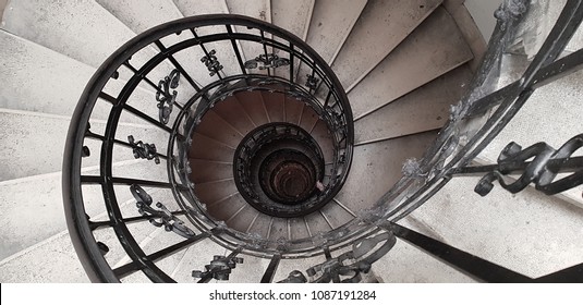 A spiral staircase spiraling down about five floors. The winding concrete stairs are empty. The metal hand rail is nicely decorated. The image approaches the golden ratio and Fibonacci spiral. 