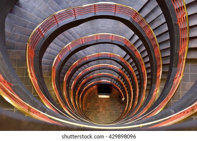 Spiral Staircase With Warm Light And Red Bannister