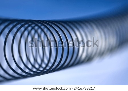 Spiral steel wire with selective focus and blurred blue sky background. Part of a cattle fence in Sauerland, Germany. Graphic structure with focus on the curled metal. Symbol or flexibility, infinity