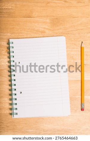 Spiral-bound lined notebook is lying open on wooden tabletop, with yellow pencil resting parallel. Stationery, writing, education, office supplies, creative process, organization, minimalistic