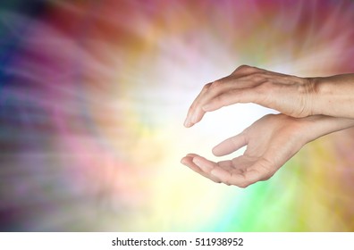 Spiraling Healing Energy - female hands held in gently cupped position with a spiraling swirl of colors behind and radiating white light streaming outwards with copy space on left side