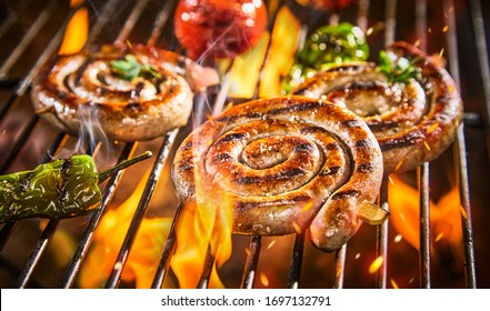 Spirals of spicy sausage grilling on a BBQ over hot flaming coals with chili peppers and tomatoes in close up - Shutterstock ID 1697132791