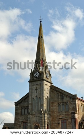 Spire and Clock on Old Stone Church seen against Blue Sky 
