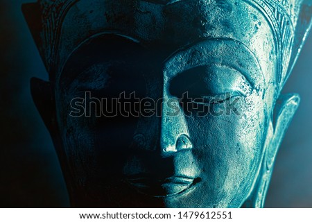 Spiriitual enlightenment. Enlightened buddha face statue close-up. Bold graphic image with atmosperic blue tone light and star highlight. Religious lifestyle awakening via meditation. Serene power.