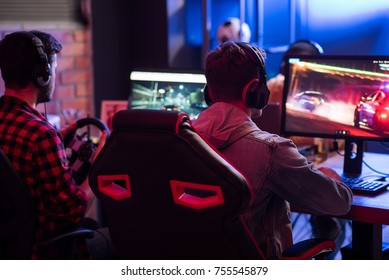 Spirit Of Competition. Back View Of Young Guys Are Concentrated On Car Racing Video Game While Sitting At Home And Using Modern Computer. Selective Focus