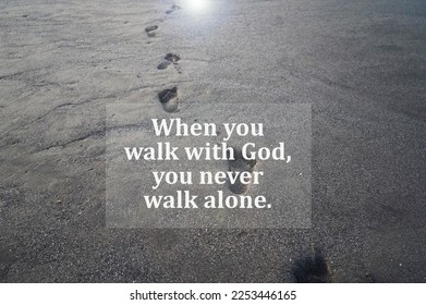 Spiritual inspirational quote - When you walk with God, you never walk alone. With footprints on beach black sand background. Believe in God concept.