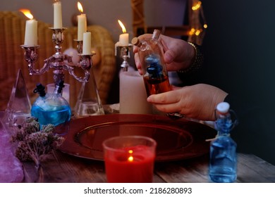 spiritualistic session in salon of soothsayer, fortune-teller, hands of female medium, alchemist, herbalist hold witchcraft potion, poison, elixir of youth, burning candles, spells, ritual magic - Shutterstock ID 2186280893