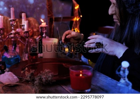 spiritualistic session in salon of soothsayer, witches, herbalists, fortune-teller, hands of female medium make magical passes over red dish of water, burning candles, spells, rituals black magic