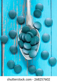 Spirulina Tablets Algae Nutritional Supplement On Silver Spoon Placed On Turquoise Wooden Background, Vertical Image, Close Up To, Overhead View.
