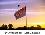 A Spitfire flying over the British Royal Air Force flag during sunset