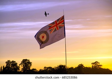 A Spitfire Flying Over The British Royal Air Force Flag During Sunset