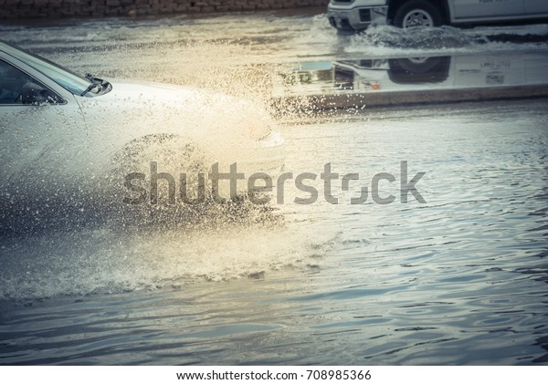 Splash by car as it goes through flood water after\
heavy rains of Harvey hurricane storm in Houston, Texas, US.\
Flooded city road big puddle spray from the wheels of sedan car\
roaring by. Vintage tone