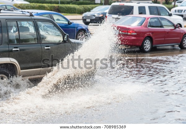 Splash by car as it goes through flood water after\
heavy rains of Harvey hurricane storm in Houston, Texas, US.\
Flooded city road with big puddle of water spray from the wheels of\
SUV car roaring by.