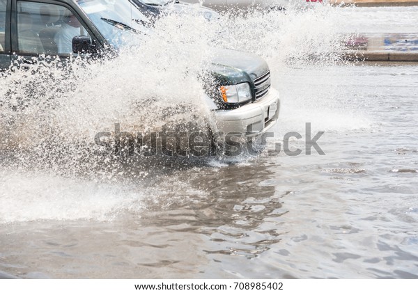 Splash by car as it goes through flood water after\
heavy rains of Harvey hurricane storm in Houston, Texas, US.\
Flooded city road with big puddle of water spray from the wheels of\
SUV car roaring by.