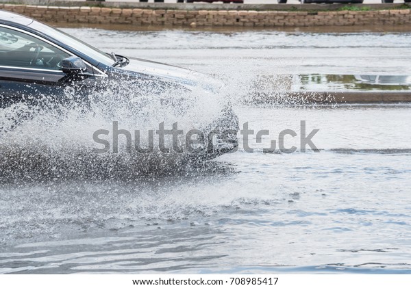Splash by car as it goes through flood water after\
heavy rains of Harvey hurricane storm in Houston, Texas, US.\
Flooded city road with big puddle of water spray from the wheels of\
sedan car roaring by