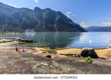 Splash In The Calm Waters Of A Spectacular Norwegian Fjord As Someone Jumps Off A Shore Side Diving Board, Sunbathers On A Rocky Beach, Eidfjord, Hardangerfjord, Hordaland, Norway 07.12.19