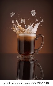 Splash Of  Ice Coffee Drink On A Brown Background. Refreshing Iced Cappuccino Liquid Drink Pouring Into A Mug, Cup With Ice Cubes. Cold Beverage Wave. Close-up Design Liquor Milk, Coffee And Ice.  