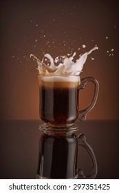 Splash Of  Ice Coffee Drink On A Brown Background. Refreshing Iced Cappuccino Liquid Drink Pouring Into A Mug, Cup With Ice Cubes. Cold Beverage Wave. Close-up Design Liquor Milk, Coffee And Ice.  