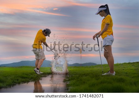 splash of the water in channel raceway of the golf course, hit golf ball away to destination on the green by golf player, along with golf-mate or competitor in an exciting beside in background