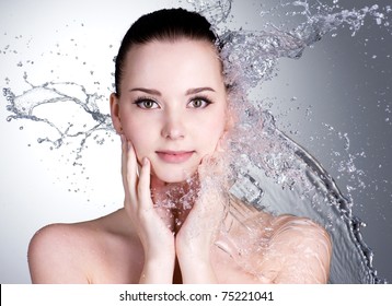 Splashes of water on the beautiful face of young woman - grey background