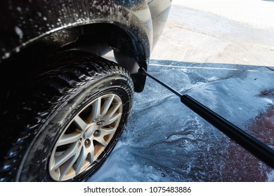 Splashes of water with soap fly in different directions from a stream of a high pressure. The man washes hand car wash with water under pressure in the car wash outside in the hangar for car wash.