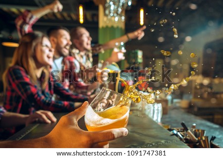 Splashing beer in the foreground and in focus. Sport, people, leisure, friendship and entertainment concept - happy football fans or male friends drinking beer and celebrating victory at bar or pub