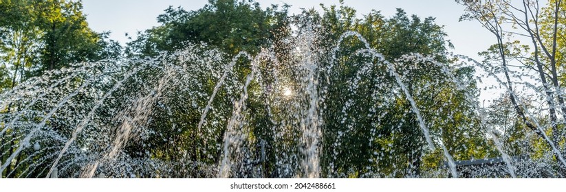 Splashing Water In The Fountain At Summer City Public Urban Park. Water Jets Abstract Image Close-up. Thin Jets Of Pure Clear Aqua Splashes Flying Upwards Under Pressure.