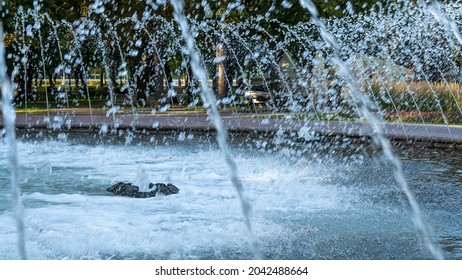 Splashing Water In The Fountain At Summer City Public Urban Park. Water Jets Abstract Image Close-up. Thin Jets Of Pure Clear Aqua Splashes Flying Upwards Under Pressure.