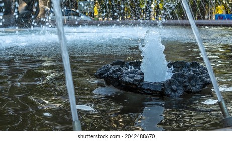 Splashing Water In The Fountain At Summer City Public Urban Park. Water Jets Abstract Image Close-up. Thin Jets Of Pure Clear Aqua Splashes Flying Upwards Under Pressure.