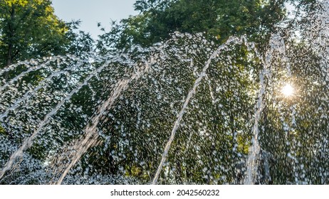 Splashing Water In The Fountain At Summer City Public Urban Park. Water Jets Abstract Image Close-up. Thin Jets Of Pure Clear Aqua Splashes Flying Upwards Under Pressure.