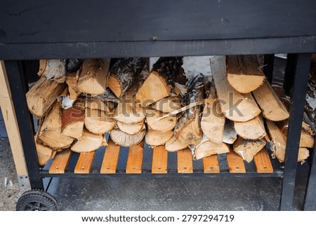 Split birch logs neatly stacked on a slatted wooden shelf supported by a black metal frame. The scene shows cut wood with pale bark and exposed grain, some pieces with peeling