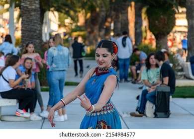 SPLIT, CROATIA - Jun 09, 2021: A Female Street Artist Performs Traditional Asian Dance With Hand Gestures In Daylight With Green Trees And People In The Background In Split, Croatia