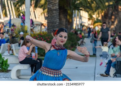 SPLIT, CROATIA - Jun 09, 2021: A Female Street Artist Performs Traditional Asian Dance With Hand Gestures In Daylight With Green Trees And People In The Background In Split, Croatia