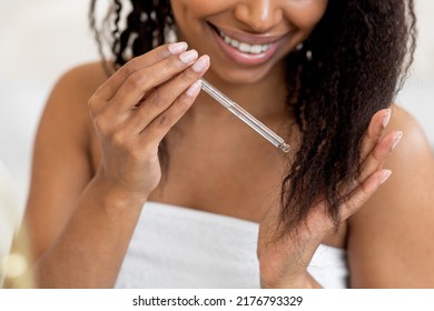 Split Ends Care. Smiling African American Woman Applying Moisturising Oil To Her Curly Hair, Closeup Of Young Black Female Putting Haircare Product With Dropper While Making Beauty Routine At Home