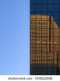 Split perspective of a clear blue sky and the mirrored glass exterior of a modern skyscraper reflecting another nearby building