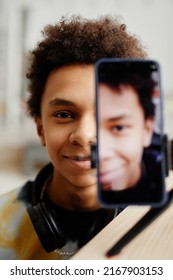 Split Portrait Of Smiling Black Teenager Filming Video For Social Media, Focus On Smartphone Screen