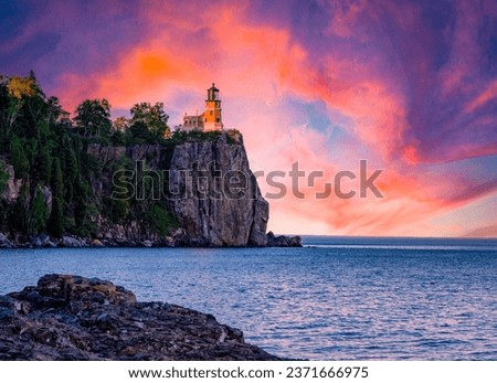 The Split Rock lighthouse at the edge of a waterside cliff under the orange and blue shaded sunset sky