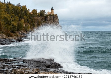 Split Rock lighthouse in Minnesota under grey sky.  Large rock bluff with blue and green water splash in foreground.  Motion blur action water against wet rocks.  