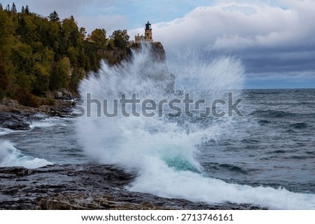 Split Rock lighthouse in Minnesota under grey sky.  Large rock bluff with blue and green water splash in foreground.  Motion blur action water against wet rocks.  